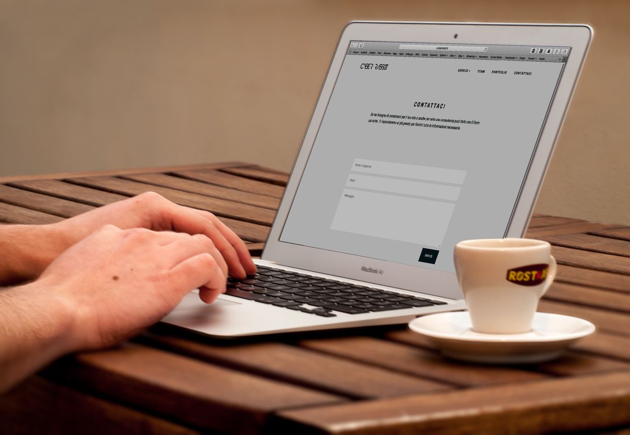 Close-up view of hands typing on a laptop beside a cup of coffee resting on a wooden desk.